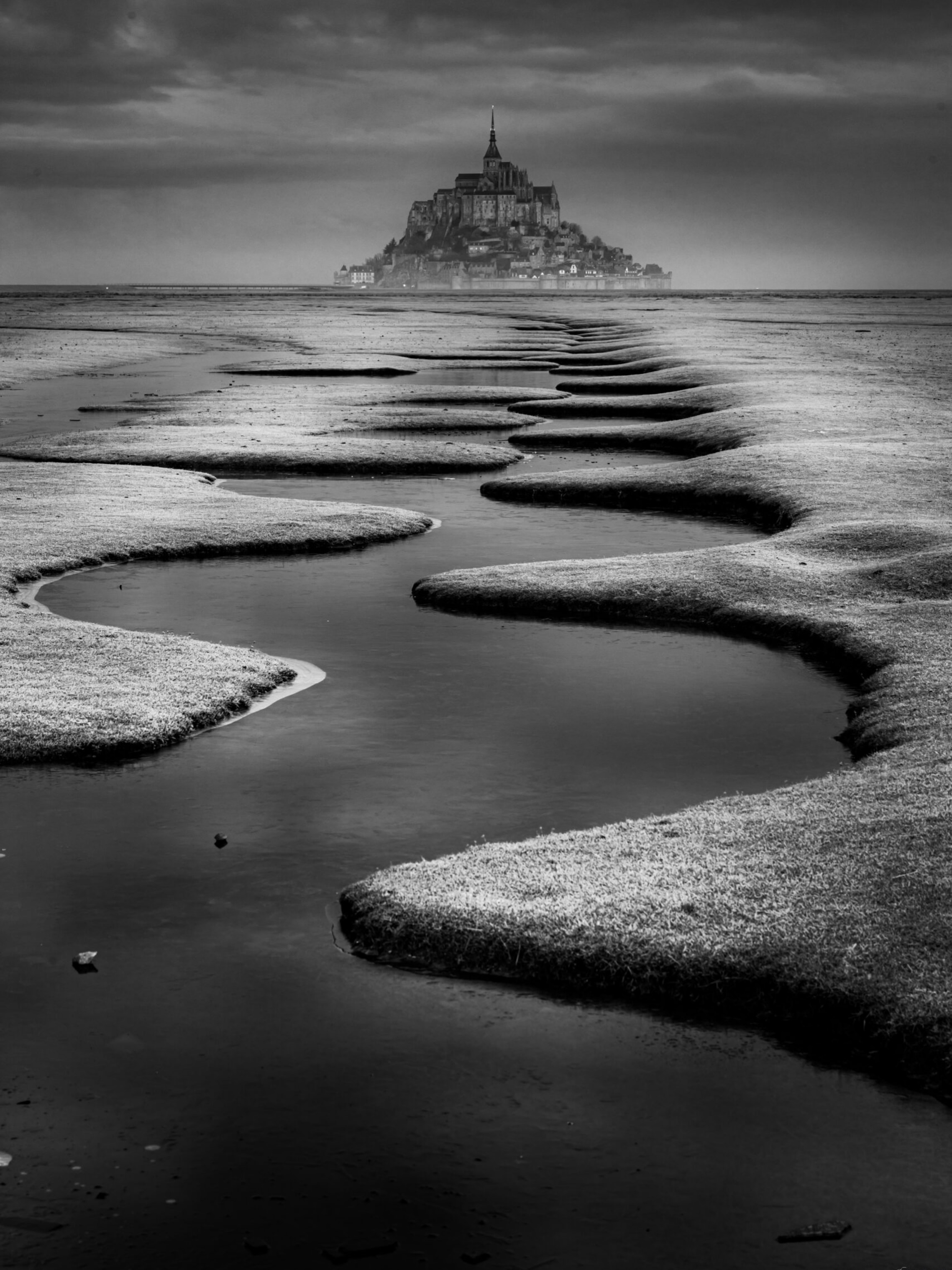 Ce matin la, face au Mont-Saint-Michel, tout était calme. Le ciel pesait lourd, la mer s’était retirée loin au large, et il ne restait plus que ces lignes dans les méandres, comme un chemin qui guidait le regard jusqu’au Mont.

Il y a des paysages qu’on photographie… et d’autres qu’on garde avec soi longtemps après être rentré.

#MontSaintMichel #Bretagne #NoirEtBlanc #InstantBreton